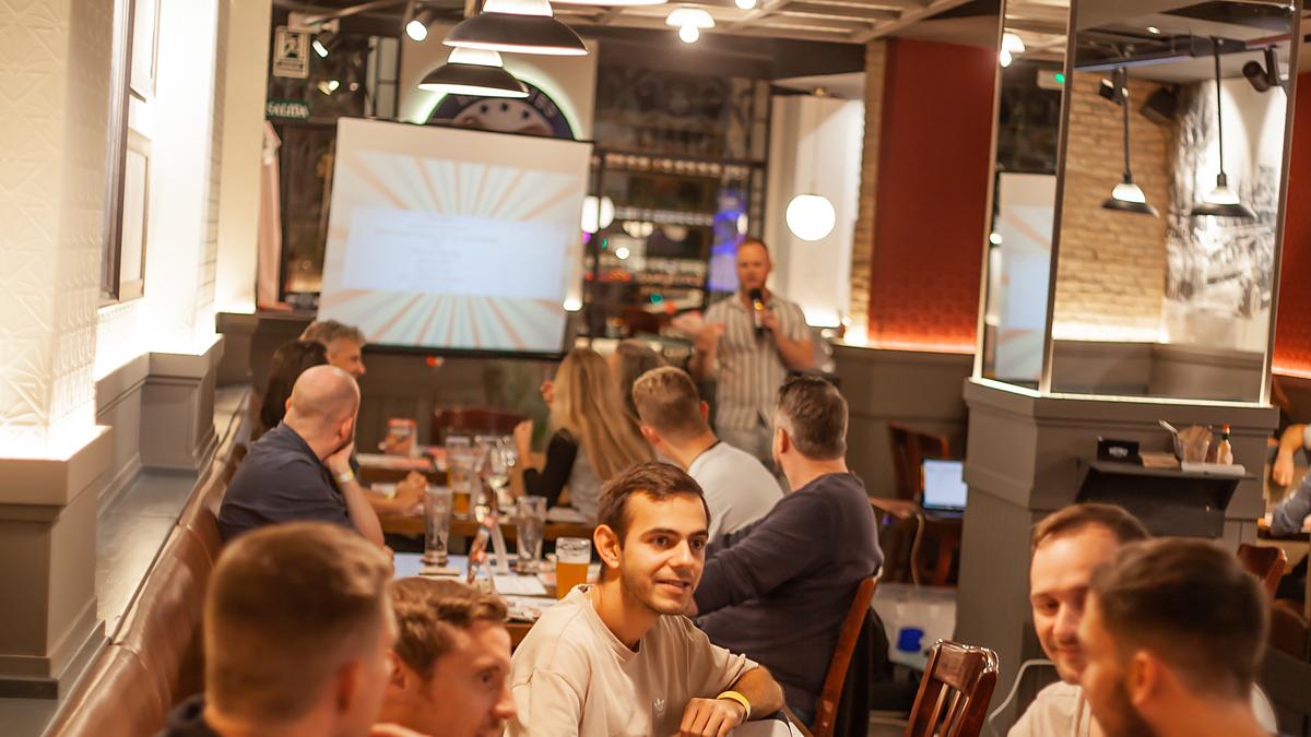 A host with a microphone running a trivia night for teams at their tables